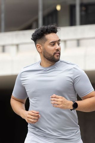 Male runner jogging in urban concrete landscape wearing gray tee and smartwatch training