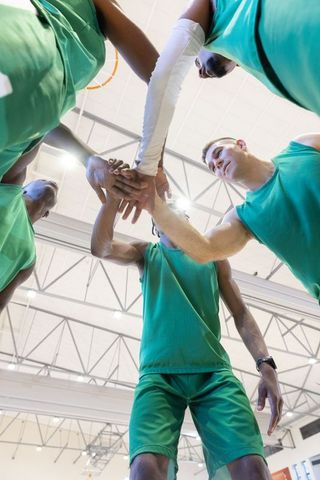 Diverse basketball team huddling and stacking hands, unity and focus in indoor gym