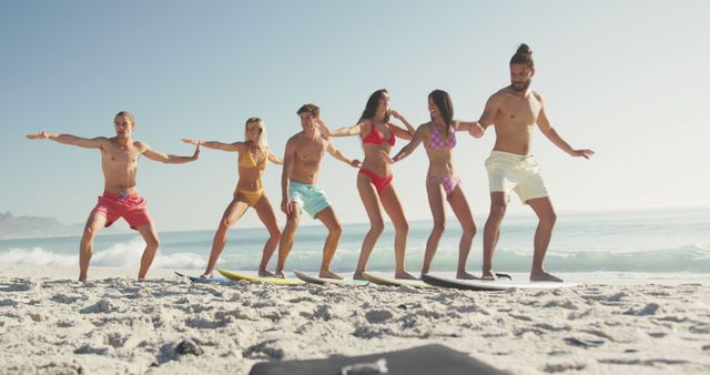 Group of friends wearing swimwear standing on surfboards in sandy beach with ocean waves in background. Perfect for promoting summer vacations, beach resorts, surfing schools, and active lifestyles.