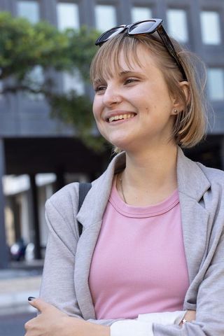 Smiling young professional standing in city wearing blazer and sunglasses holding papers