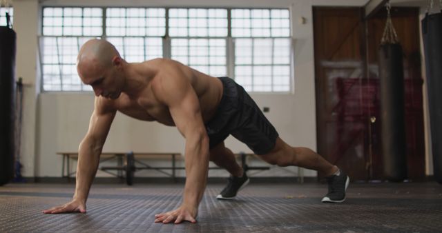 Shirtless bald man performing wide push-ups on gym floor, displaying strength and fitness. Ideal for use in workout-related content, fitness blogs, gym promotions, and exercise tutorials.