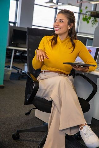 Confident woman in 30s presenting data on tablet while gesturing in modern office meeting
