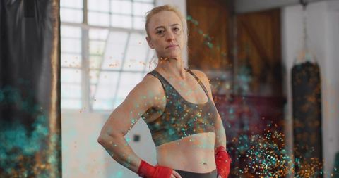 Confident female boxer posing in gym with red hand wraps and turquoise energy particles