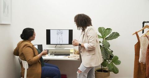Two designers collaborating over garment sketch and fabric swatches at small studio workstation