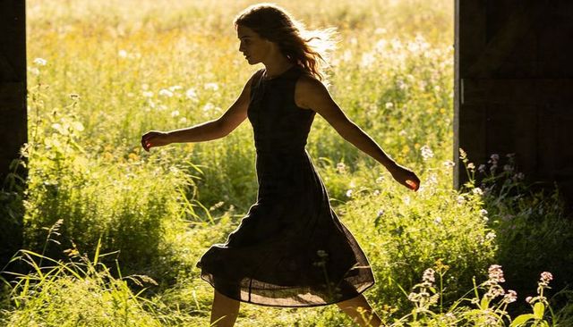 Walking woman exiting barn into sunlit meadow, backlit silhouette golden hour wildflowers