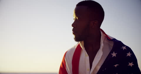 Pensive Man Wrapped in American Flag at Sunset Beach