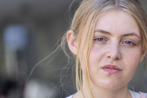 Close-up contemplative blonde woman gazing in urban background with freckles and blue eyes