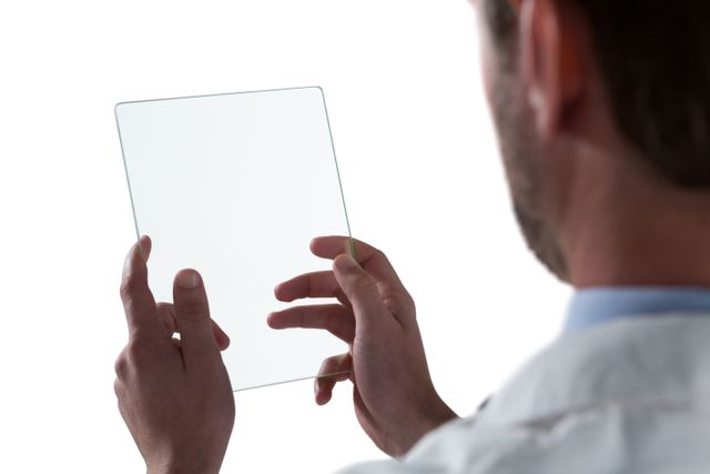 Male doctor holding and using a transparent glass digital tablet against a white background. This image can be used to represent modern medical technology, innovation in healthcare, and futuristic digital devices. Ideal for use in healthcare technology advertisements, medical websites, and educational materials about advancements in medical tools.