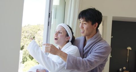 Sunlit morning romance: diverse couple wearing bathrobes pointing at garden view