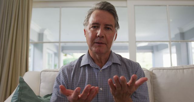 Senior caucasian man talking and gesturing during a image call, sitting in living room. retirement lifestyle with communication technology at home.