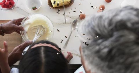 Grandparent Guiding Child Whisking Batter Over Marble Countertop