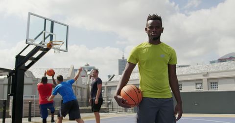Diverse men playing basketball on outdoor court in bright clothing
