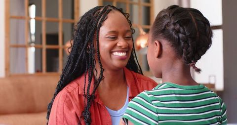African american mother and daughter smiling and talking while sitting on living room sofa