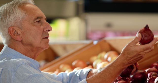 Senior man choosing fresh onion in grocery store. This image can be used for content related to healthy eating, seniors shopping, grocery store experiences, and promoting healthy lifestyles. It is ideal for articles about senior citizens prioritizing nutritious diets, as well as advertisements for grocery stores and fresh produce.