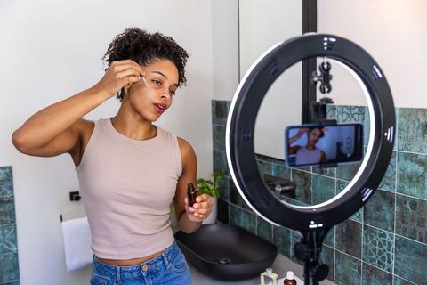 African american woman applying facial serum recording skincare tutorial with ring light