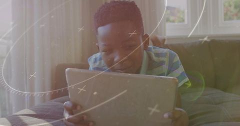 African American boy watching tablet on couch with glowing screen and lens flare