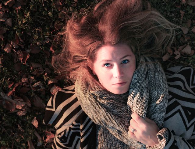 Young woman lying on autumn leaves, wrapped in a cozy blanket. Ideal for autumn season advertisements, outdoor lifestyle blogs, fashion promotions, and relaxation-themed marketing. Captures serenity and the essence of fall.
