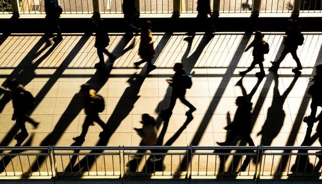 Commuters walking on sunlit pedestrian overpass casting long dramatic shadows