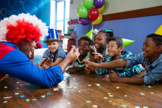 Clown showing feather to children sitting at desk during birthday