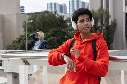 Young man in red hoodie adjusting smartwatch while listening to headphones on urban rooftop