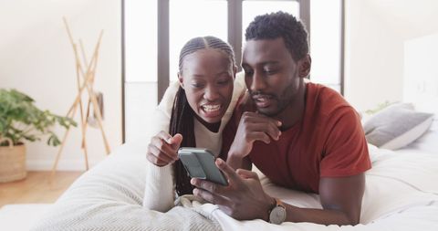 Happy Couple in Bedroom Sharing Fun Moments on Smartphone