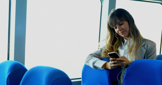 Young woman is using smartphone while sitting on public transport. Suitable for topics on technology use, public transport, commuting, and communication. Can be used for blog posts, advertisements, or articles related to mobile technology, travel, and urban lifestyles.