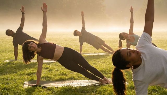 Group practicing sunrise yoga side-plank in misty park backlit morning wellness