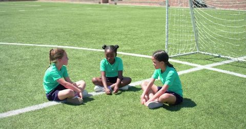 Girls sitting and talking on soccer field near goal demonstrating teamwork and friendship