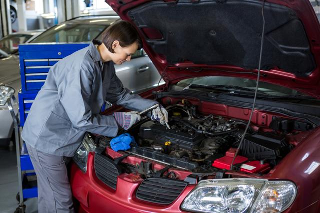 Female mechanic checking oil level in car engine with a dipstick at a repair garage. Ideal for illustrating automotive services, gender diversity in technical professions, and car maintenance tutorials.