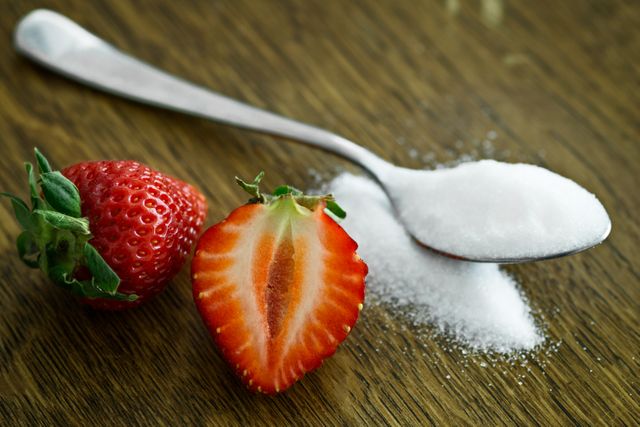 High-quality image of fresh strawberries next to a spoonful of sugar on a wooden table conveys natural sweetness and healthiness. Perfect for use in food blogs, recipe websites, nutritional articles, and health-related advertisements.