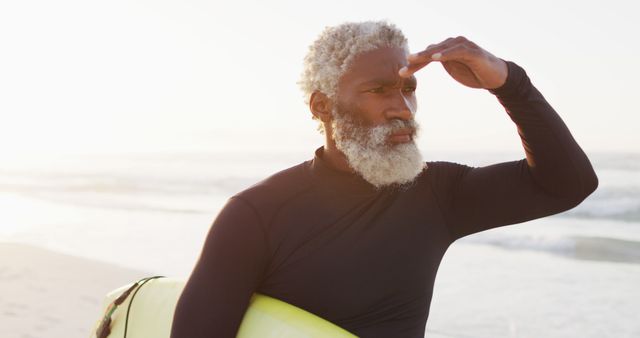 Happy senior african american man walking with surfboard on sunny beach. healthy and active time beach holiday.