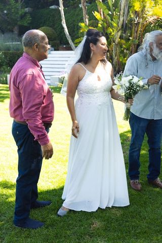 Bride holding bouquet speaking with senior indian family member and guest at garden wedding celebrat