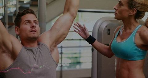 Female trainer guiding male athlete performing overhead pull-ups at gym