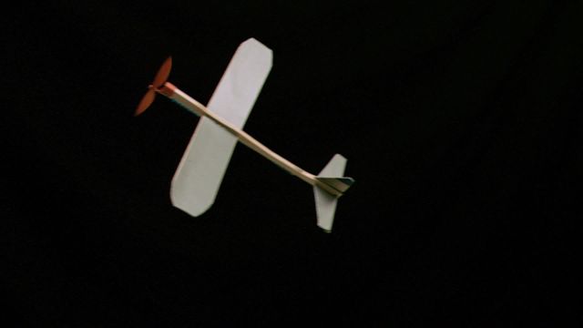 Wooden plane with a propeller in mid-flight captured in super slow motion against a black background. Useful for themes related to aviation, simplicity, childhood toys, flight mechanics, or educational purposes. Ideal for websites, promotional materials, educational content, and presentations focused on the physics of flight and toy designs.