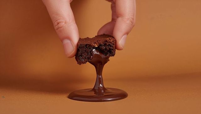 Pinching hand holding bitten brownie dripping glossy melted chocolate into pool