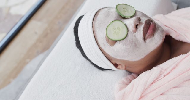 Woman relaxing at spa with facial mask and cucumber slices on eyes is perfect image for promoting beauty treatments, self-care routines, or wellness services. Ideal for use in marketing materials for spas, skincare products, and relaxation or health-related content.