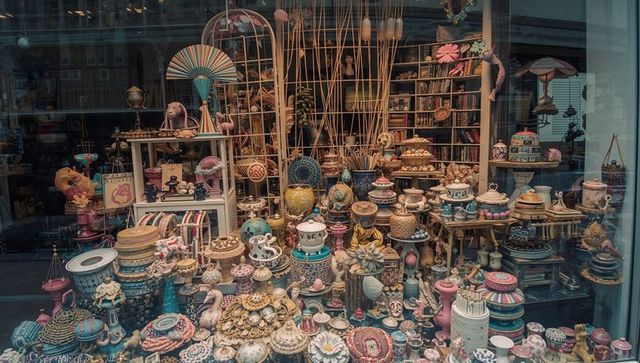 Showcasing densely packed pastel ceramic display in ornate storefront window with vintage teapots