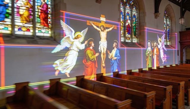 Projection mapping crucifixion and saints illuminating cathedral nave and wooden pews