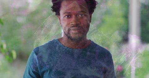 Contemplative man standing behind smudged glass on porch with garden bokeh reflections