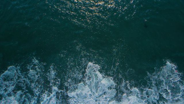 Aerial ocean surface churning with breaking waves, white foam and deep blue texture