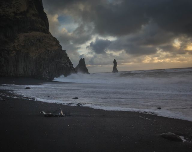 The coastline captures dark, moody atmosphere of Reynisfjara Beach's crashing waves and towering basalt columns. Useful for tourism content, travel magazines, nature blogs, advertisements targeting those seeking scenic destinations.