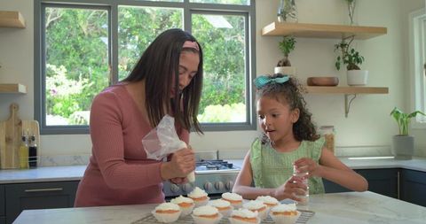 Mother and daughter decorating cupcakes together in sunlit modern kitchen, family baking