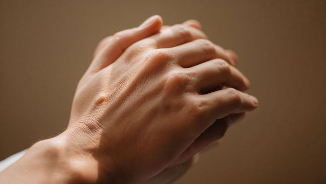 Clasping adult hands showing skin texture and veins, warm closeup with soft bokeh