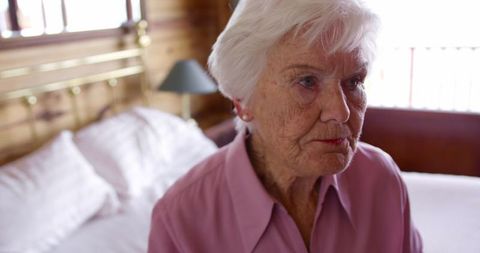 Elderly Woman Sitting on Bed Holding Medicine at Home