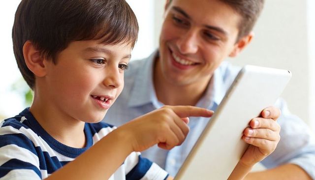 Father guiding son on tablet for learning and play, smiling family technology moment