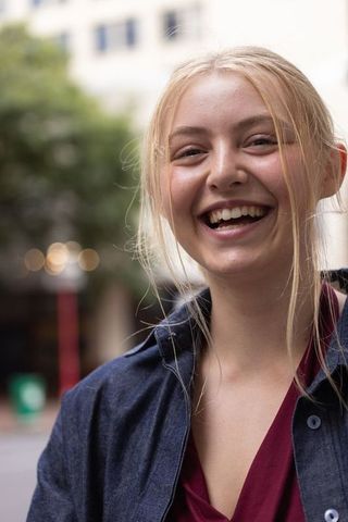 Young woman laughing on city sidewalk wearing denim jacket and burgundy top candid portrait