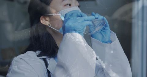 Korean clinician adjusting protective goggles over surgical mask in lab coat