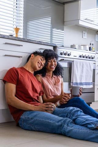 Multicultural couple sharing morning coffee on sunlit kitchen floor