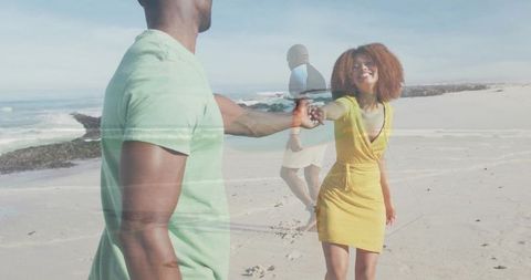 Couple holding hands walking along sunny beach woman reaching back in yellow dress