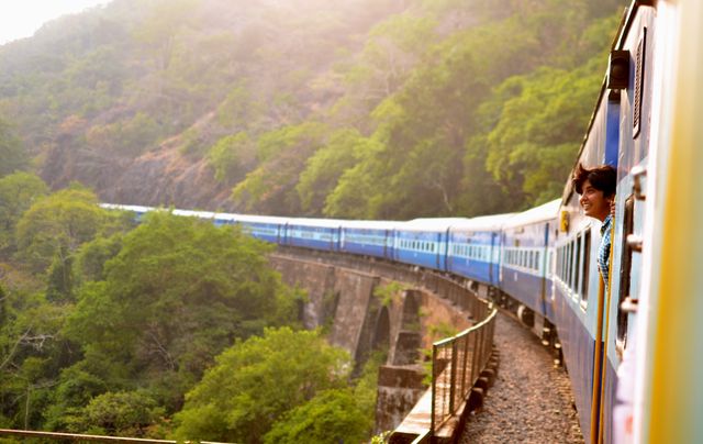 Woman looking out train window enjoying scenic view as train travels through mountainous region with lush greenery. Ideal for tourism, transportation, travel blogs, adventure advertisements, and nature exploration content.